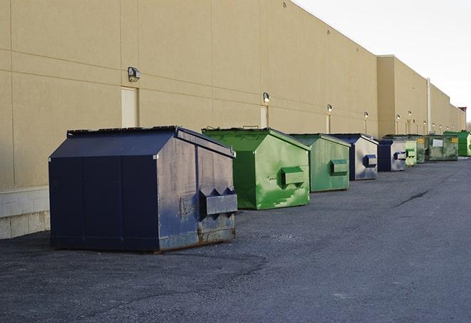 a construction worker unloading debris into a blue dumpster in Foxboro